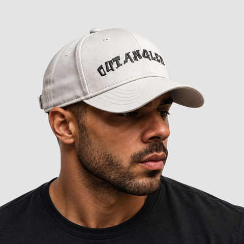 A man wearing a light gray baseball cap with 'OUTANGLED' embroidered in black across the front, shown in a close-up profile shot against a light gray background.